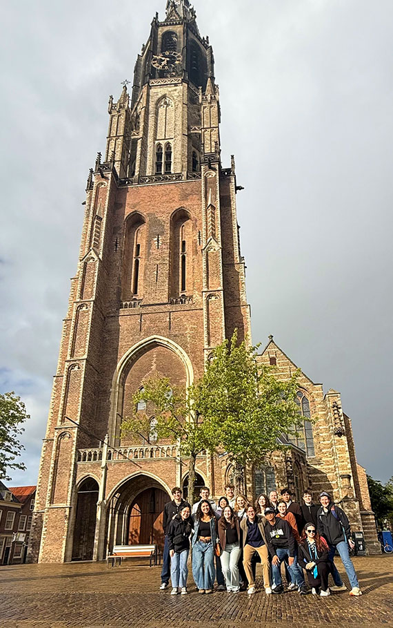 More than a dozen young adults stand outside a very old church with a tall steeple