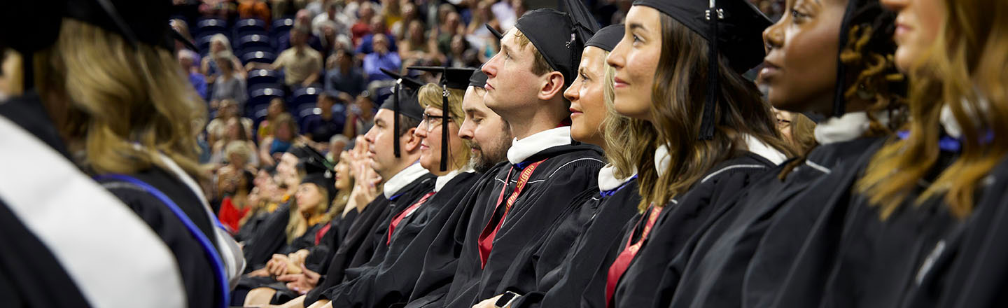 Graduates sit at commencement while listening to speaker