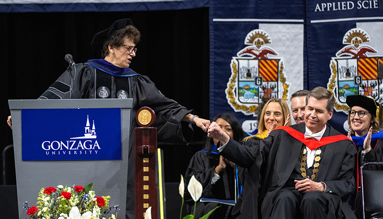 A woman at a podium fist bumps a man sitting in a chair A woman at a podium fist bumps a man sitting in a chair