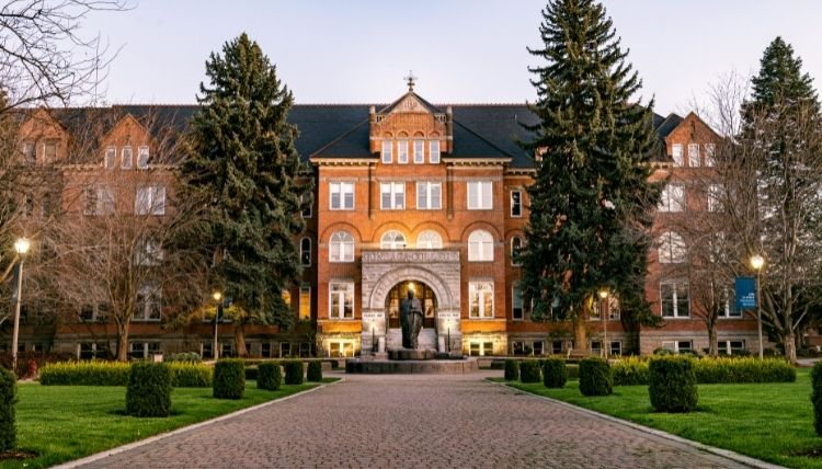 A shot of the front of College Hall, including the statue of St. Ignatius in front of the main entrance. Trees surround the building. The sun is reflecting in the windows. A shot of the front of College Hall, including the statue of St. Ignatius in front of the main entrance. Trees surround the building. The sun is reflecting in the windows.