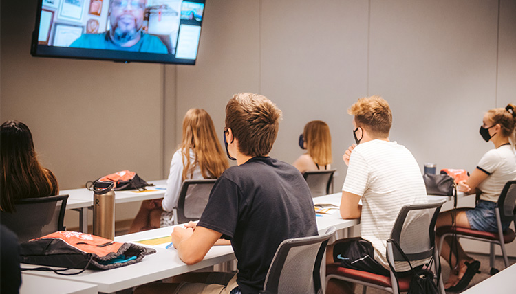 A group of students watches a speaker on Zoom in a classroom. A group of students watches a speaker on Zoom in a classroom.