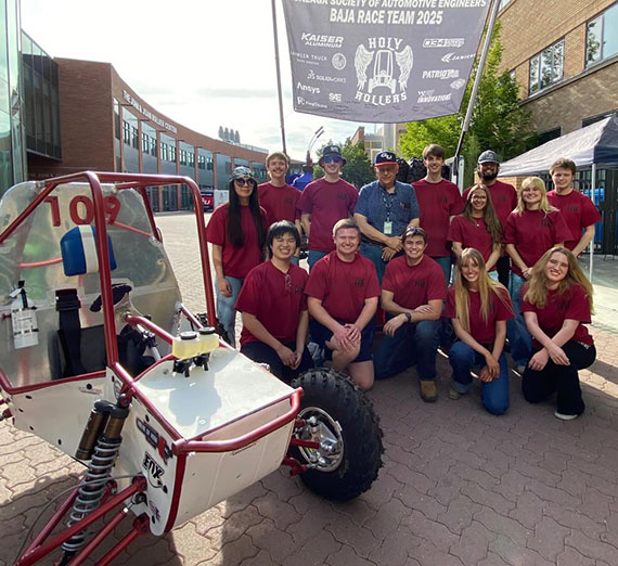 A dozen people in red t-shirts pose near a single-passenger off-road vehicle