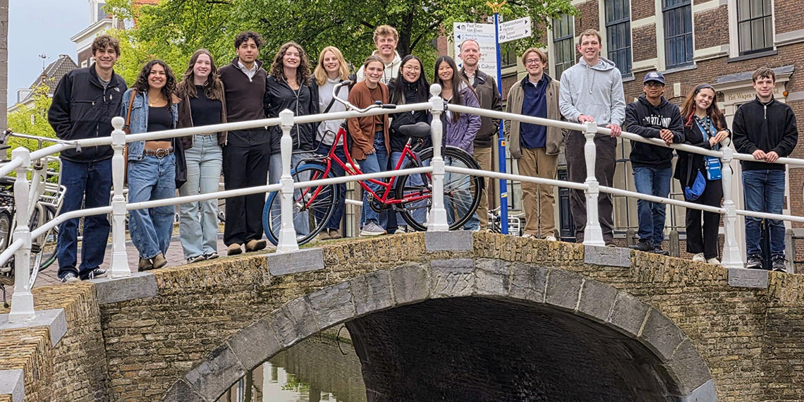 16 students stand on a bridge over a netherlands canal