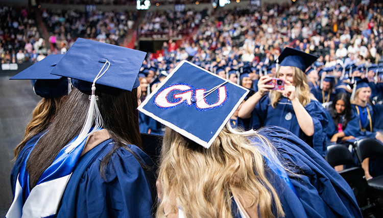 A woman in commencement regalia takes a picture of two friends A woman in commencement regalia takes a picture of two friends