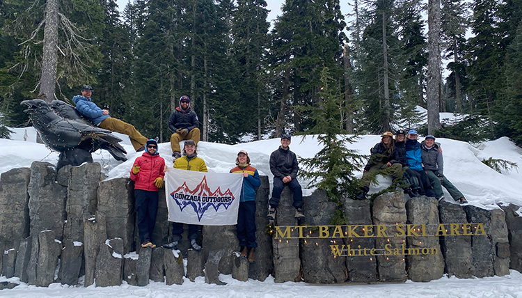 group poses with Mt Baker sign and GU Outdoors flag group poses with Mt Baker sign and GU Outdoors flag