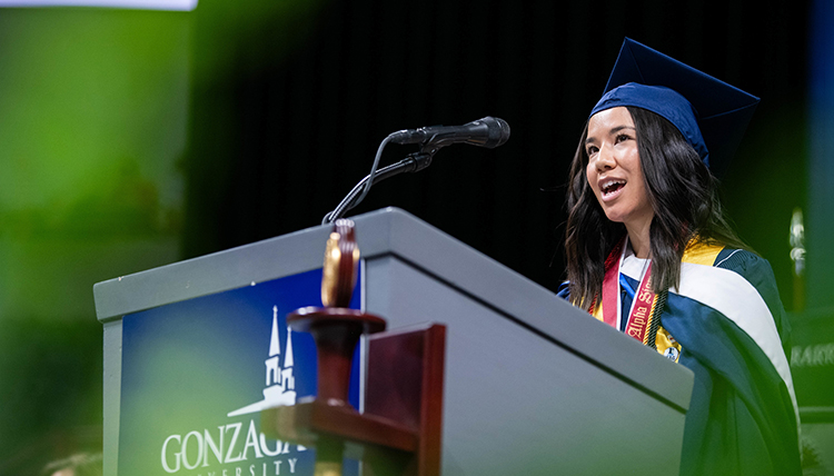 A young woman speaks at a podium while wearing a graduation cap A young woman speaks at a podium while wearing a graduation cap