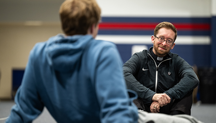 Fr. Tim Breen sits on the floor talking to a student. Fr. Tim Breen sits on the floor talking to a student.